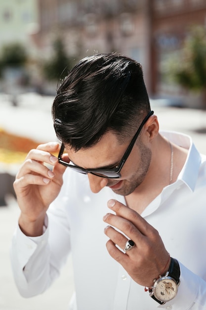 L'uomo di moda in una camicia bianca è in piedi per strada in una giornata di sole è in posa guardando con gli occhiali