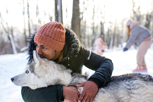 L'uomo di razza mista abbraccia il suo cane husky nel parco forestale invernale