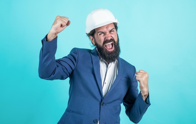 L'uomo di successo con barba e baffi nel casco sembra uomo d'affari in cantiere, celebra il successo.