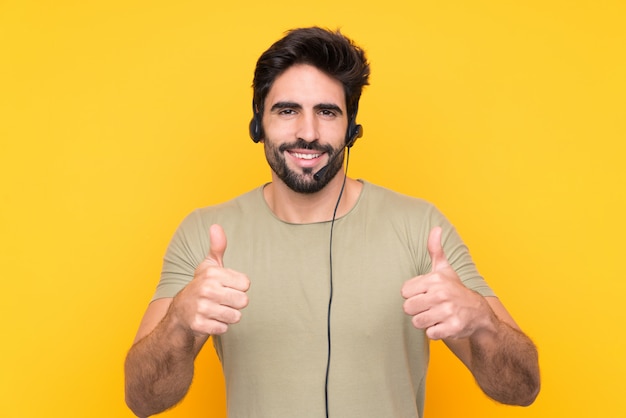 L'uomo di Telemarketer che lavora con una cuffia avricolare sopra la parete gialla isolata dando pollici aumenta il gesto