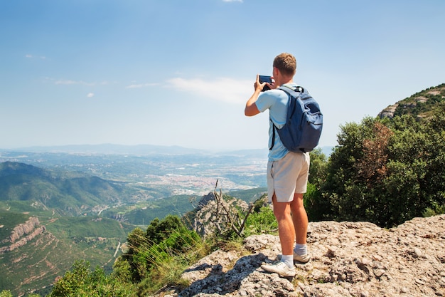 L&#39;uomo di viaggio con la condizione dello zaino prende una foto dallo spazio di Sunny Day dello smartphone Mountians