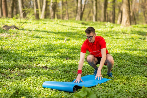 L'uomo diffonde una stuoia di yoga blu in un parco sull'erba verde per esercizi e relax. Uno stile di vita sano