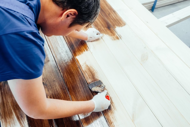 L'uomo dipinge le tavole di legno con il pennello Falegname ebanista vernicia la superficie in legno Flusso di lavoro autentico