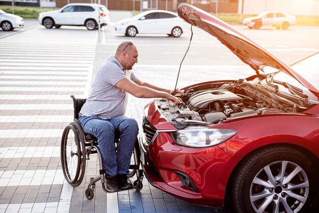 L'uomo disabile in sedia a rotelle controlla il motore della sua auto al parcheggio