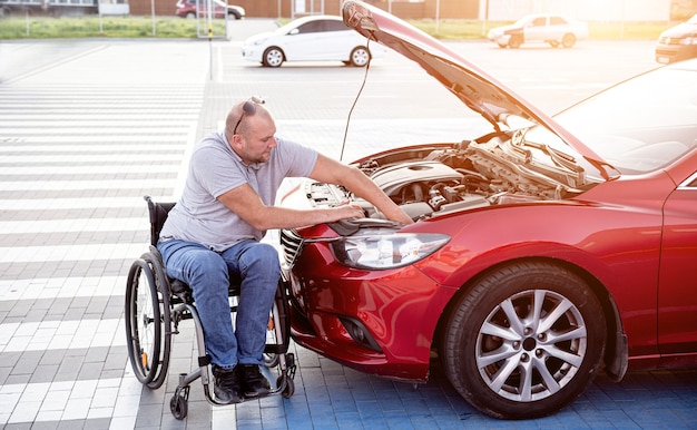 L'uomo disabile in sedia a rotelle controlla il motore della sua auto al parcheggio