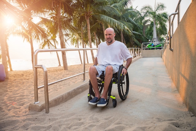 L'uomo disabile in sedia a rotelle si muove su una rampa verso la spiaggia.