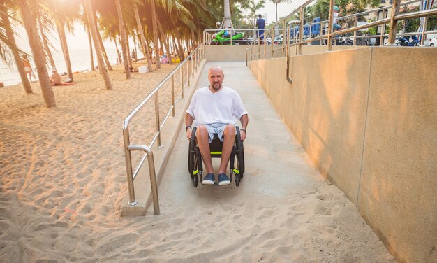 L'uomo disabile in sedia a rotelle si muove su una rampa verso la spiaggia.