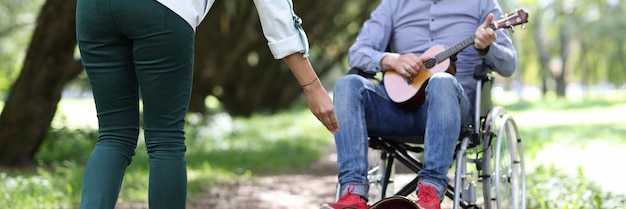 L'uomo disabile in sedia a rotelle suona la chitarra nel parco e fa soldi il musicista di strada disabile