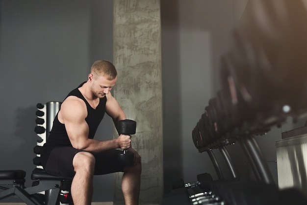 L'uomo e il suo personal trainer si esercitano con i manubri in palestra. Ragazzo muscoloso che sostiene il suo amico sull'attrezzatura di sollevamento pesi, copia spazio