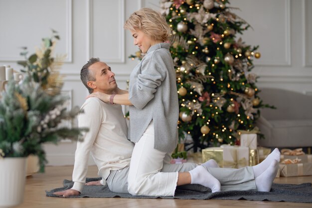 L'uomo e la donna adulti si siedono sul pavimento vicino all'albero di Natale e si abbracciano