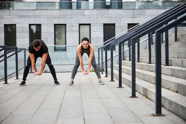 L'uomo e la donna atletici felici si piegano mentre si scaldano prima dell'allenamento sulle scale all'aperto