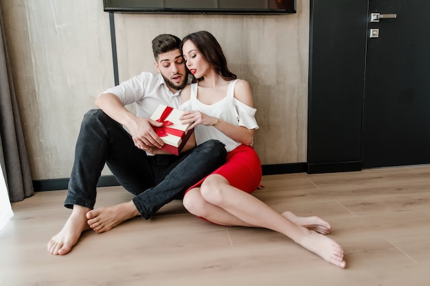 L'uomo e la donna bei delle coppie si siedono a casa con il presente in contenitore di regalo a casa