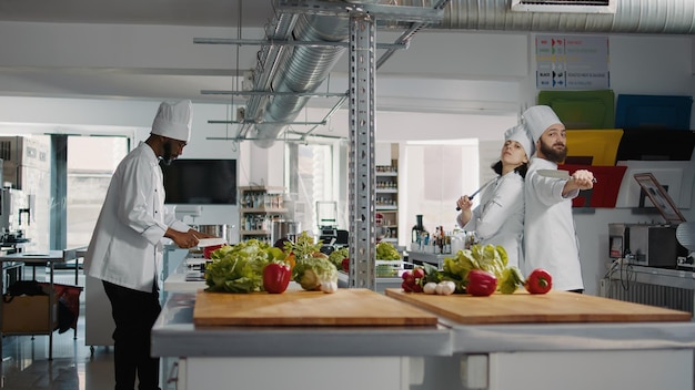 L'uomo e la donna cuochi si comportano in modo divertente con i coltelli in cucina, pubblicizzando preparazioni di pasti professionali. Team di chef che si sentono allegri e utilizzano ingredienti biologici per cucinare pasti gourmet.