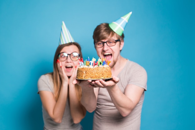 L'uomo e la donna divertenti del nerd stanno portando i cappucci ed i vetri di feste che tengono la torta di compleanno con le candele