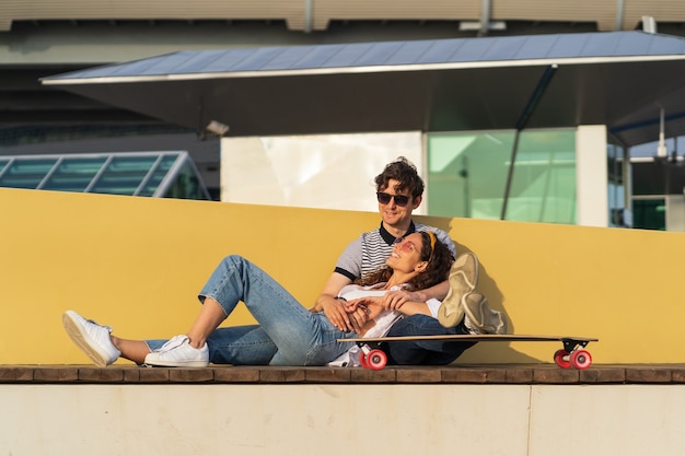 L'uomo e la donna eleganti si godono il tramonto coccole a longboard rilassandosi dopo aver fatto skateboard nello skate park