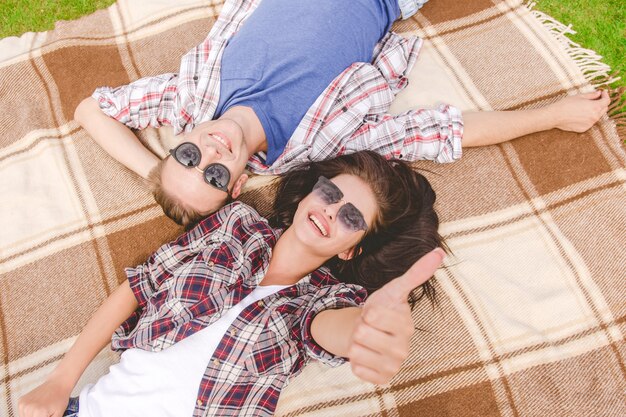 L'uomo e la donna felici con gli occhiali da sole giacciono e fanno gesti a terra