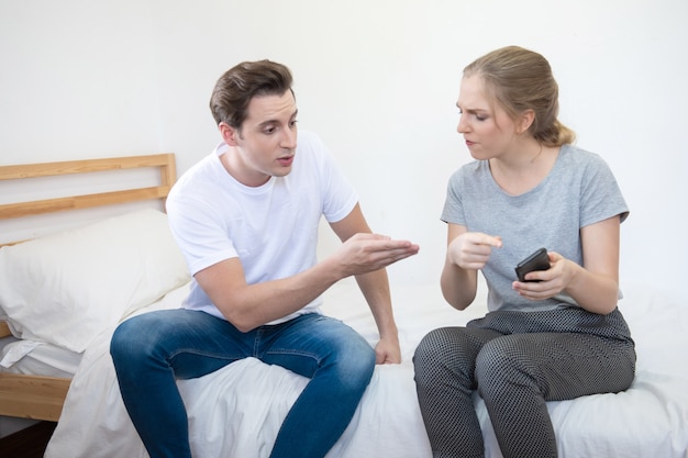 L'uomo e la donna infelici caucasici discutono sul telefono cellulare astuto nella casa, concetto sociale di problema di relazione con lo spazio della copia.
