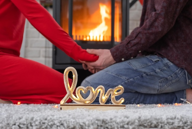 L'uomo e la donna innamorati a casa sono seduti vicino alla stufa del camino con un fuoco ardente su un tappeto accogliente San Valentino coppia felice storia d'amore relazioni