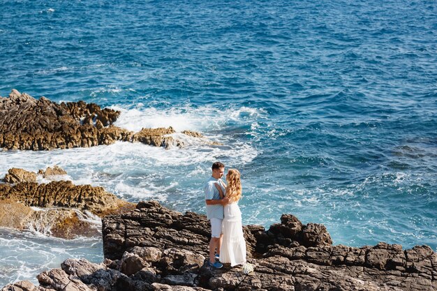 L'uomo e la donna innamorati stanno abbracciando e tenendosi per mano sulla spiaggia rocciosa