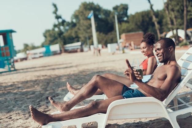 L&#39;uomo e la donna sono sdraiati sui lettini e bevono cocktail