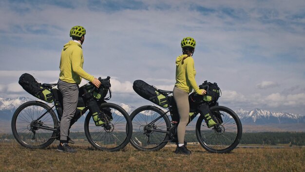 L'uomo e la donna viaggiano su terreni misti cicloturismo con bikepacking. Le due persone viaggiano con le borse della bicicletta. Montagna innevata.