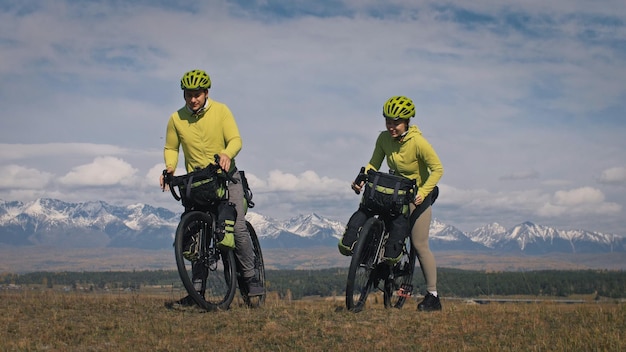 L'uomo e la donna viaggiano su terreno misto cicloturismo con bikepacking Le due persone viaggiano con borse da bicicletta Sport bikepacking abbigliamento sportivo da bici nei colori verde nero Montagna innevata