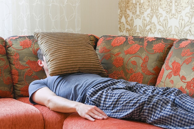 L'uomo è sdraiato sul divano in depressione. sdraiato sul divano coperto da un cuscino.