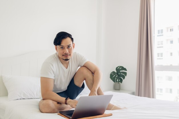 L'uomo è seduto sul letto e lavora al suo laptop.