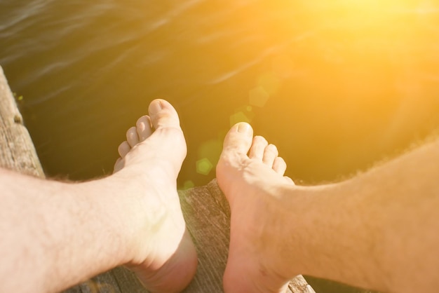 L'uomo è seduto sul molo di legno Foto rustiche e naturali all'aperto Estate fiume Gambe da vicino