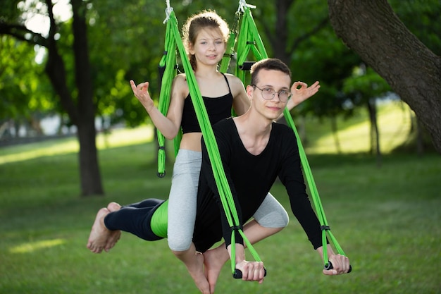 L'uomo e una bambina fanno yoga di gruppo su un'amaca nel parco