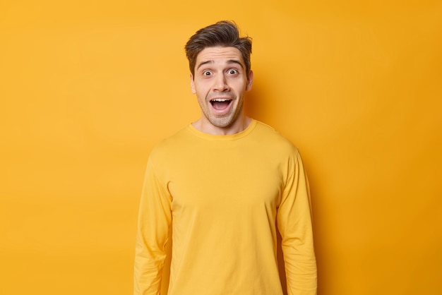 L'uomo europeo sorpreso e iperemotivo urla di piacere e la sorpresa tiene la bocca aperta vestito in pose casual da maglione su sfondo giallo stupito da grandi notizie lo racconta ad un amico