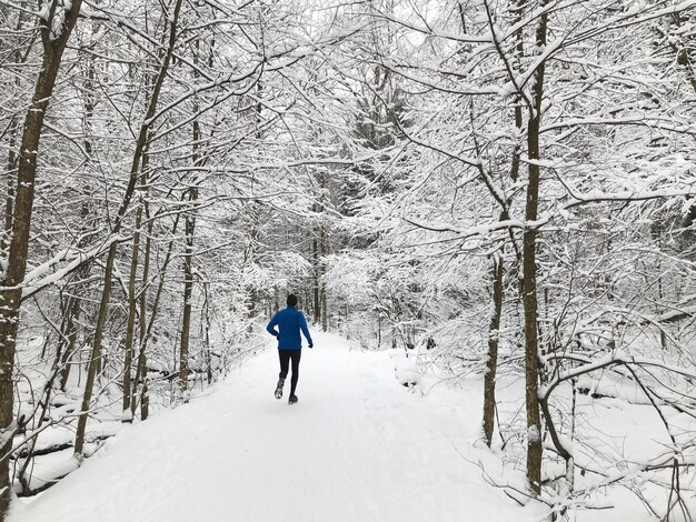 L'uomo fa jogging in una foresta invernale, correndo su strade innevate, attività all'aperto, vita sana