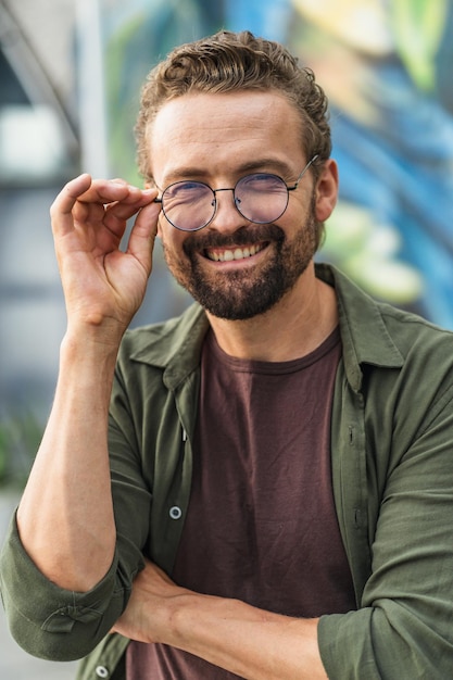 L'uomo felice con un sorriso caloroso che tiene gli occhiali con un'espressione gioiosa irradia positività e contentezza