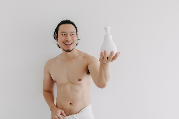 L'uomo felice indossa un asciugamano e tiene in mano una grande bottiglia di prodotto per la cura della pelle