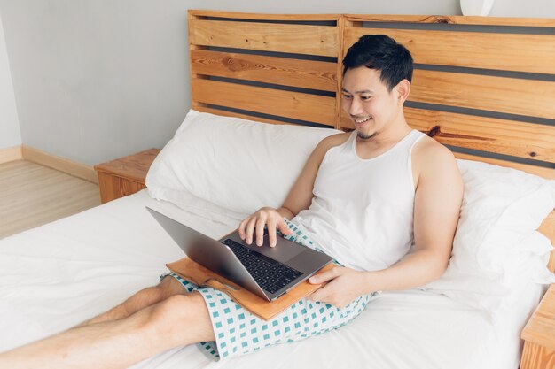 L'uomo felice sta lavorando con il suo computer portatile sul suo letto. Concetto di stile di vita libero professionista.