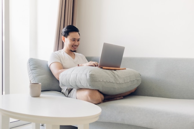 L'uomo felice sta lavorando sul divano nel concetto di lavoro a casa.