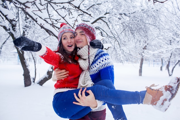 L'uomo felice tiene la sua ragazza tra le braccia nella foresta invernale