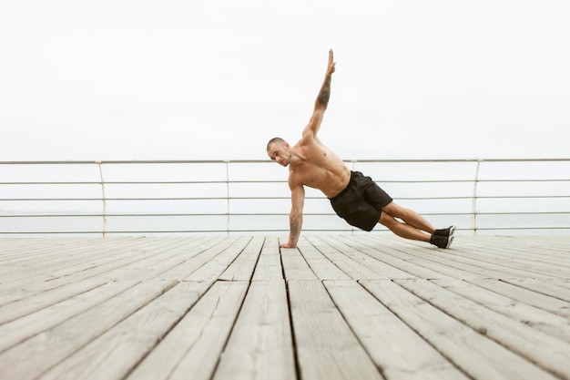 L'uomo fitness pratica hatha yoga, allena la plancia laterale Vasisthasana, equilibra la posa in spiaggia. Concetto di stile di vita sano