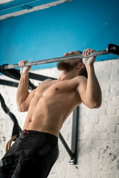 L'uomo forte che fa la tirata aumenta sulla barra orizzontale in palestra