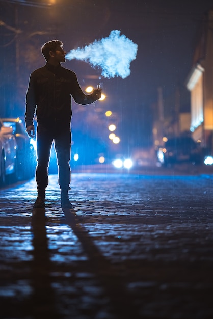 L'uomo fuma sigaretta elettronica in strada. Serata notturna