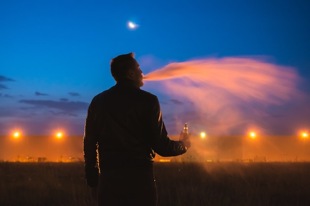 L'uomo fuma sigaretta elettronica vicino all'edificio. sera notte