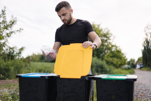 L'uomo getta nel cestino per il riciclaggio pulire il contenitore di plastica vuoto di colore diverso dei cassonetti per il riciclaggio