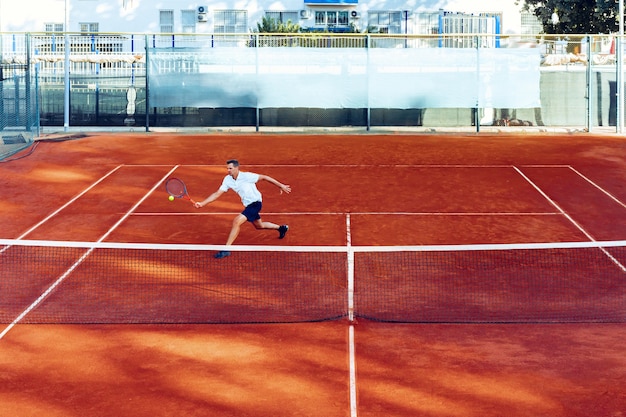 L'uomo gioca a tennis sul campo da tennis in terra battuta vista da lontano