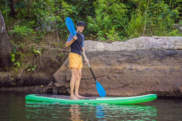 L'uomo gioioso sta allenando la tavola SUP nel fiume in una mattina di sole Stand up paddle boarding fantastiche attività ricreative all'aperto