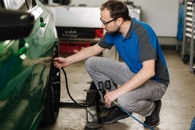 L'uomo gonfia le gomme di un meccanico di servizio auto con gli occhiali ispeziona l'auto in garage