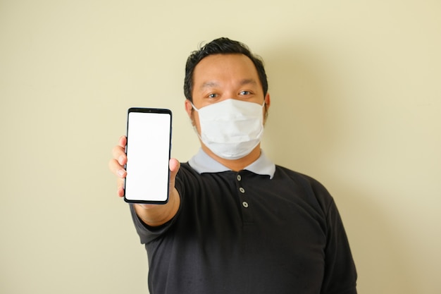 L'uomo grasso che indossa una maschera indica il suo smartphone con uno sguardo serio. gesto puntato. sfondo blu