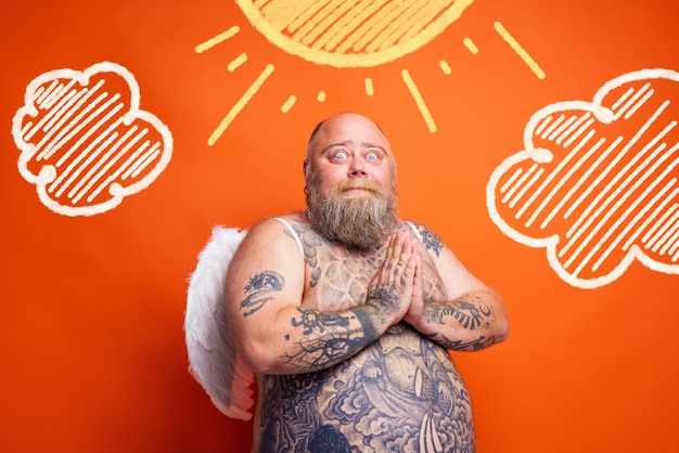 L'uomo grasso e stupito con barba tatuaggi e ali si comporta come un angelo
