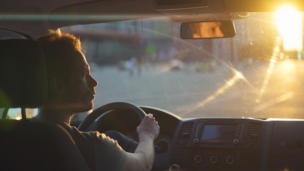 L'uomo guida l'auto in autostrada sullo sfondo del cielo al tramonto
