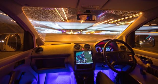 L'uomo guida l'auto nella città della pioggia. Traffico a sinistra. Serata notturna
