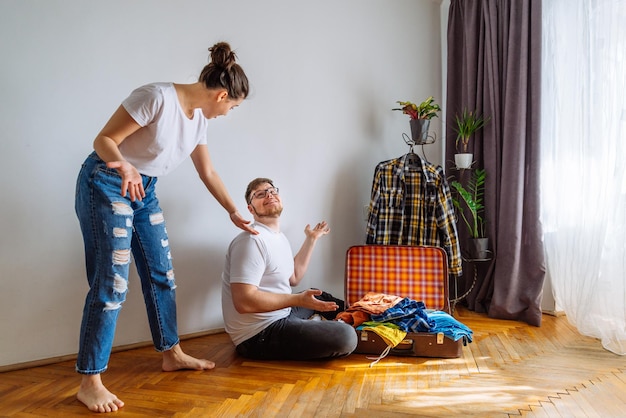 L'uomo ha bisogno dell'aiuto della donna nell'imballaggio. concetto di viaggio. uomo che cerca vestiti in forma nella borsa da viaggio.